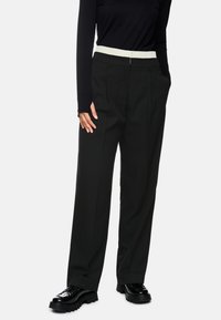 Black wide-leg trousers with a textured cream elastic waistband, featuring side pockets and a sleek, tailored design.