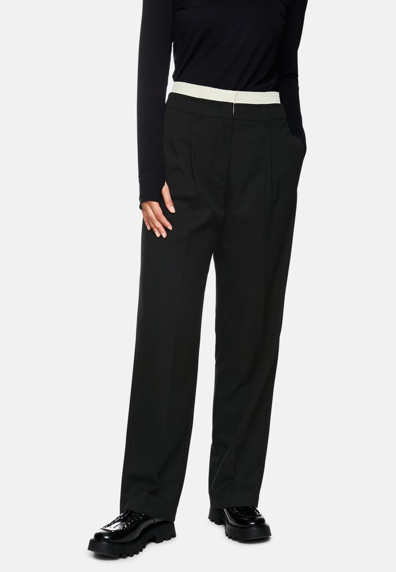 Black wide-leg trousers with a textured cream elastic waistband, featuring side pockets and a sleek, tailored design.