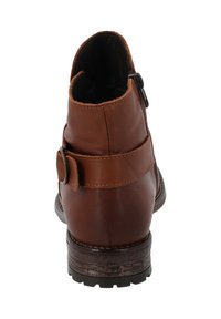 Bota de tobillo de cuero marrón con punta redondeada, cremallera lateral y una correa decorativa con hebilla. Suela de goma texturizada para un buen agarre.