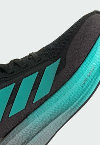 Scarpa sportiva nera con accenti turchesi e tessuto testurizzato. Presenta tre strisce turchesi e una suola trasparente contrassegnata "LIGHTBOOST."