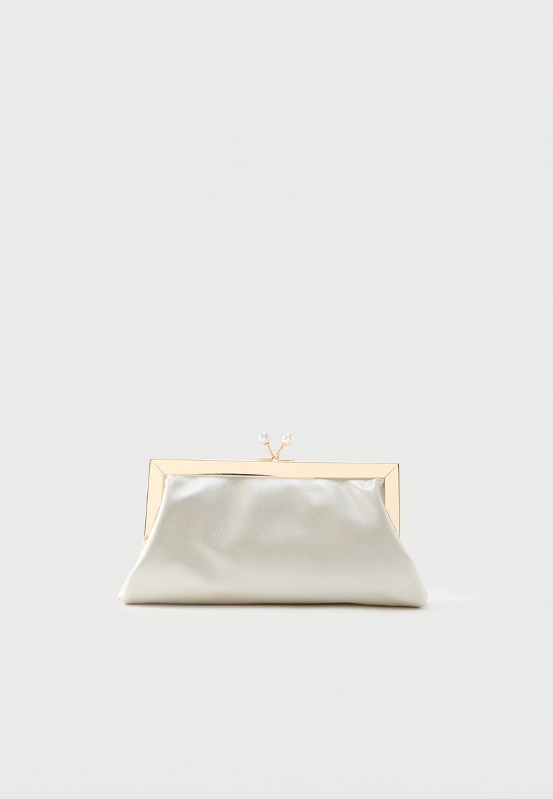 Petit sac à main argenté brillant avec une monture dorée et deux fermoirs ronds sur le dessus, posé sur un fond clair uni.