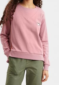 Rosa sweatshirt med en texturerad v-ringning, ribbade ärmslut och nederkant. Har en liten broderad koppgrafik på bröstet. Matchar med gröna byxor.