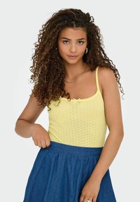 Top giallo a maglia con spalline sottili e un dettaglio a fiocco davanti, abbinato a una gonna in denim scuro. Design testurizzato e aderente.