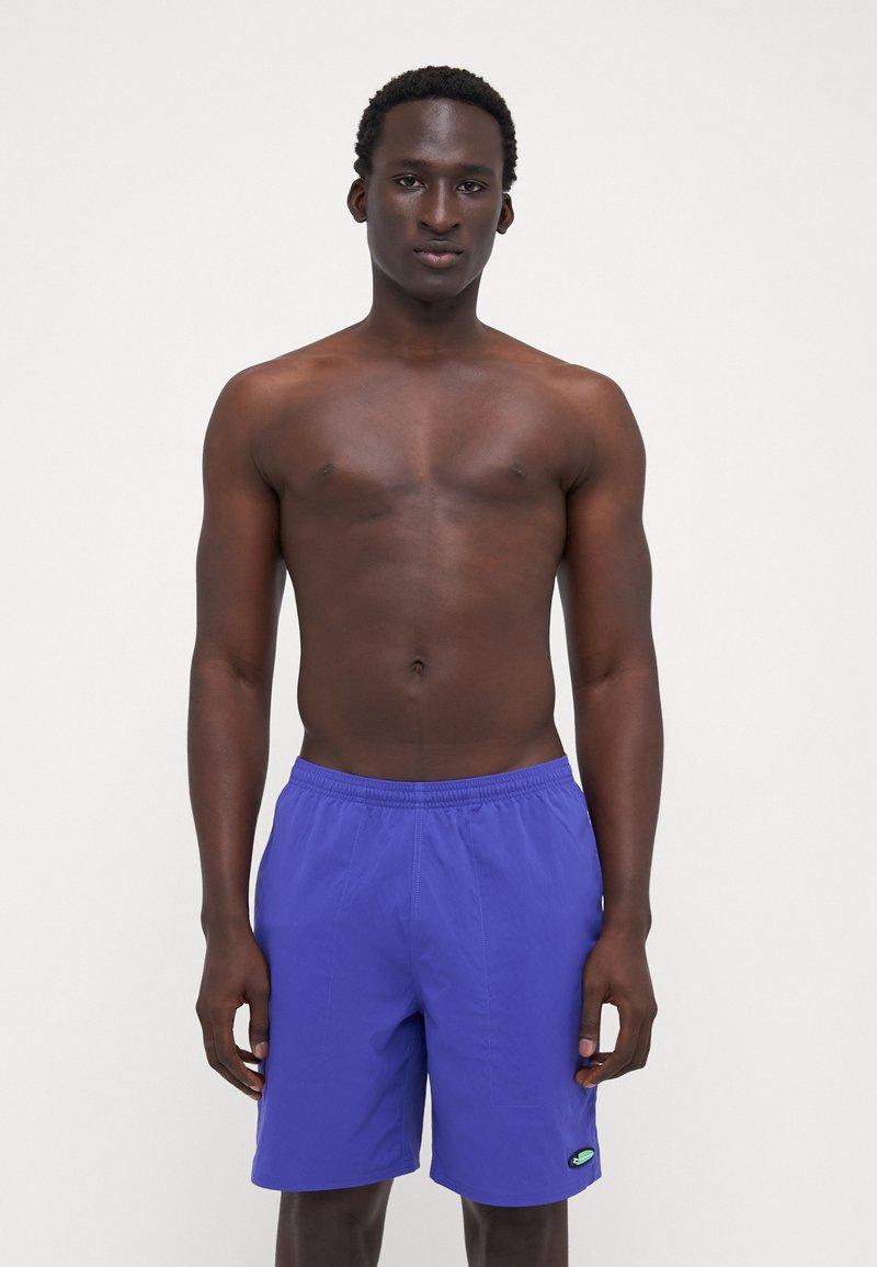 Purple swim shorts with an elastic waistband and side pockets, featuring a small logo accent. Lightweight fabric texture.