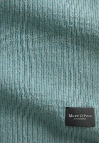 Textiel in lichtblauw, ribbelstructuur. Heeft een zwart label met witte tekst "Marc O'Polo" en "EST. IN STOCKHOLM."