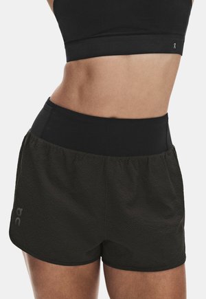 Sportbekleidung, die den Mittelteil einer Person zeigt, die einen schwarzen Sport-BH und strukturierte schwarze, hoch taillierte Laufshorts trägt.