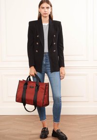 Blazer nero doppiopetto, top a righe, jeans e mocassini. Porta una borsa a tracolla rossa con manici neri e dettagli del logo.