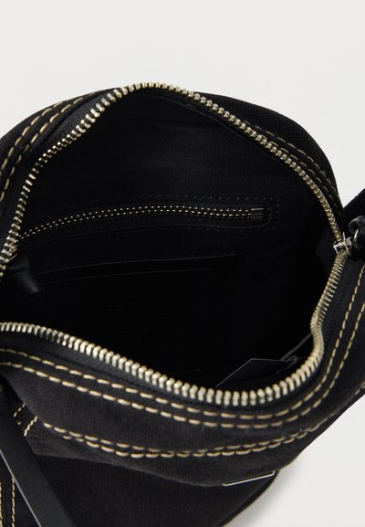 Schwarzer Stoffbeutel mit beigen Nähten, geöffnetem Reißverschluss, der eine innere Reißverschlusstasche und ein schwarzes Innenfutter zeigt.