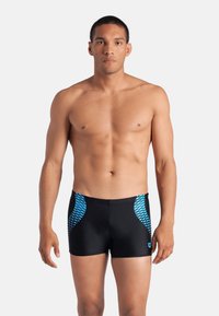 Costume da bagno neri realizzati in materiale sintetico, con motivi geometrici blu sui lati. Il design è aderente e sportivo.