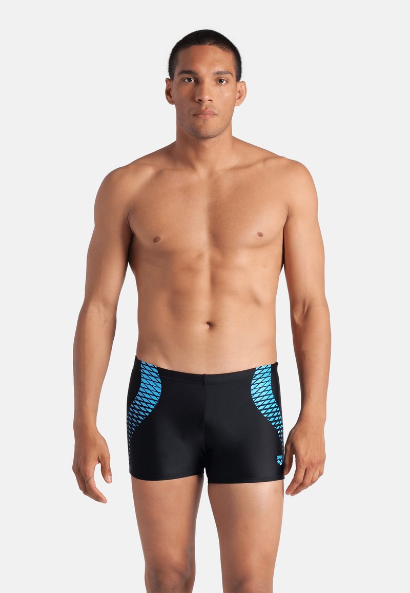 Costume da bagno neri realizzati in materiale sintetico, con motivi geometrici blu sui lati. Il design è aderente e sportivo.