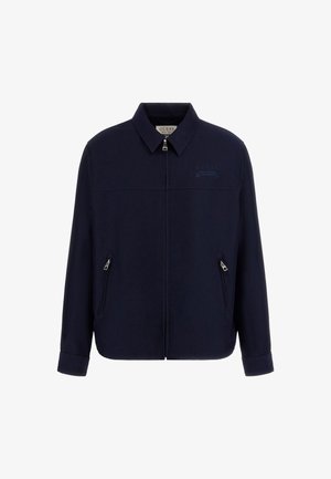 Chaqueta azul marino de tela suave. Cuenta con un cierre de cremallera frontal, dos bolsillos con cremallera y un cuello. Detalle de logo en relieve sutil.