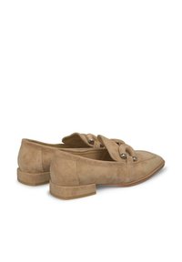Beige Wildleder-Loafer mit spitzem Zehenbereich, offenen Seiten und einem niedrigen Blockabsatz. Mit geknoteten Riemen und dezenten Metalldetails.