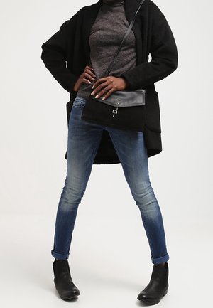 Black cardigan, gray turtleneck, blue jeans, and black ankle boots. The crossbody bag features a leather flap and metallic accents.