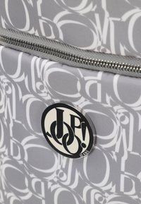 Szary materiałowy worek z białym wzorem logo, srebrnym zamkiem błyskawicznym oraz okrągłą czarno-białą naszywką marki.