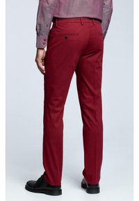 Červené kalhoty se střiháním na míru, s zadními kapsami a hladkou texturou. Kombinovány s dlouhým rukávem kostkované košile a černými botami.