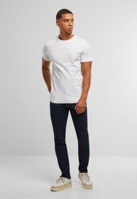 Balta īsām piedurknēm T-kreklu, apvienojot ar tumši ziliem džinsiem un gaišu krāsu sporta apaviem, ar vienkāršu, klasisku dizainu un gludu tekstūru.