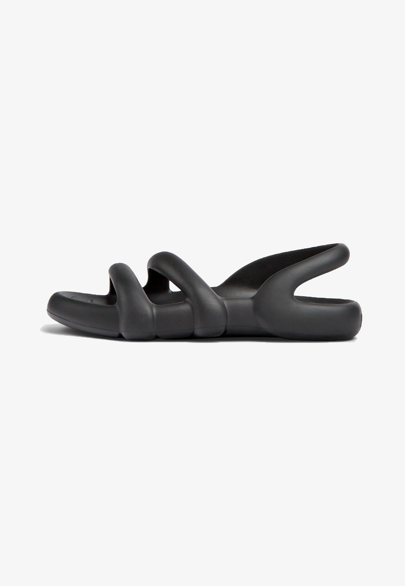 Sandales noires à enfiler avec un design ondulé, fabriquées en matériau flexible. Elles présentent des orteils ouverts et des côtés découpés pour la respirabilité.