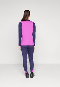 Haut de sport à manches longues avec un corps rose et des manches marine, associé à un pantalon marine avec des accents roses aux poignets. Le tissu semble lisse.