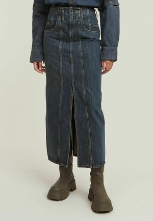 Jeanskjørt med høy midje, frontspalte og kontraststing. Mørk blå farge; glatt tekstur; kombinert med kraftige olivengrønne støvler.