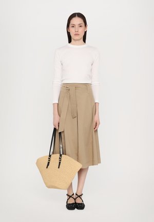 Gonna avvolgente beige con un nodo, top bianco a maniche lunghe, scarpe nere con cinturini e borsa di paglia con manici neri. Texture liscia, design casual.