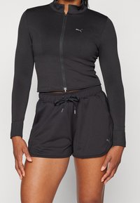 Black athletic zip-up jacket with long sleeves and high collar, paired with black drawstring shorts. Both made of smooth, stretchy fabric.