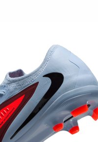 Scarpa da ginnastica azzurro chiaro con una vestibilità aderente, dotata di uno swoosh nero, accenti rossi e tacchetti arancioni su una suola semi-trasparente.