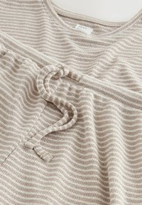 Cotton top in beige and cream stripes, featuring a rounded neckline and a tie detail at the waist. Soft, textured fabric.