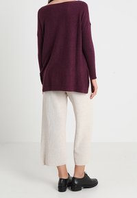 Pull en maille bordeaux avec une coupe décontractée et un large col, associé à des culottes crème claires et des chaussures noires à lacets. Texture douce évidente.