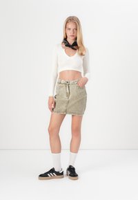 Fehér bordás cropped top V-kivágással; zöld farmer mini szoknya elülső zsebekkel; fekete sportcipő fehér részletekkel és világosszürke zoknikkal.