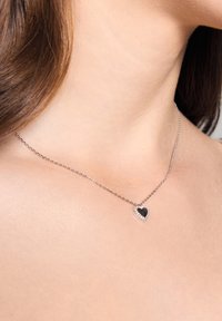 Srebrny naszyjnik z delikatnym łańcuszkiem i zawieszką w kształcie serca, z czarnym środkiem i przezroczystymi akcentami z kamieni ozdobnych.