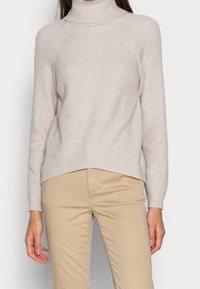 Maglione pesco chiaro a collo alto con texture a coste e maniche lunghe. Caratterizzato da una vestibilità rilassata e un design con orlo leggermente asimmetrico.