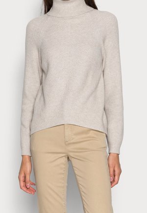 Pull à col roulé beige clair avec texture côtelée et manches longues. Présente une coupe décontractée et un design légèrement asymétrique avec un ourlet plus long à l'arrière.