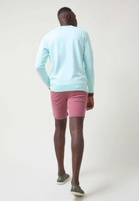 Suéter azul claro, pantalones cortos rosas y zapatillas verdes. El suéter tiene un cuello redondo, los pantalones cortos son de longitud hasta la rodilla y las zapatillas presentan una tela texturizada.