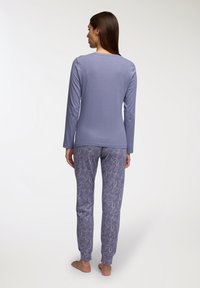 Maglietta a maniche lunghe di un lilla chiaro e pantaloni del pigiama a fantasia con design floreale in tonalità coordinate di viola e bianco. Tessuto liscio, vestibilità casual.