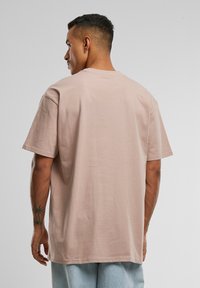 Kortærmet, lys rosa bomulds t-shirt med løs pasform, flad halsudskæring og subtil tekstur, vist fra en side- og bagperspektiv.