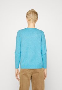 Pullover sweater in light blue, featuring a round neck and long sleeves. Soft texture with ribbed cuffs and hem. Worn over beige pants.