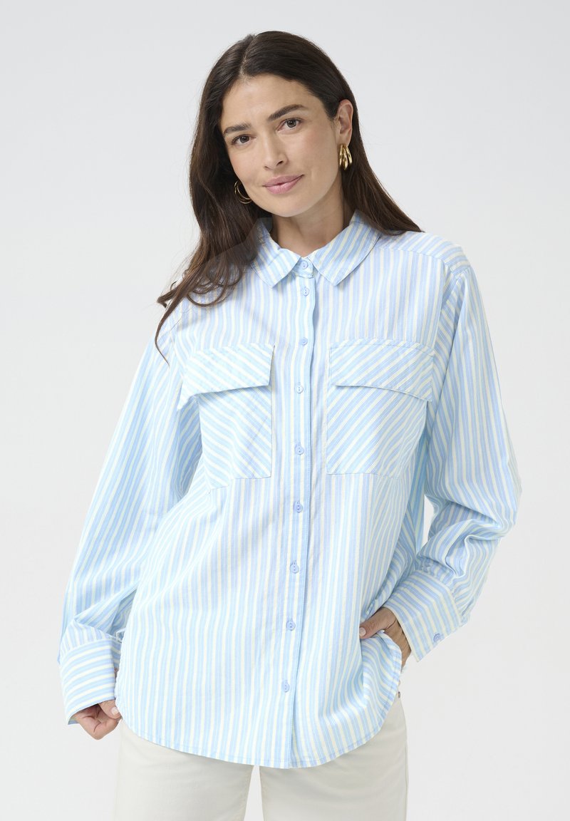 Camicia a righe azzurre e bianche realizzata in tessuto morbido, con chiusura a bottoni, colletto e due tasche sul petto. Maniche lunghe.