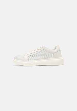 Sneakers basses blanches avec côtés en maille, lacets blancs et semelle blanche épaisse, affichées de profil sur un fond uni.