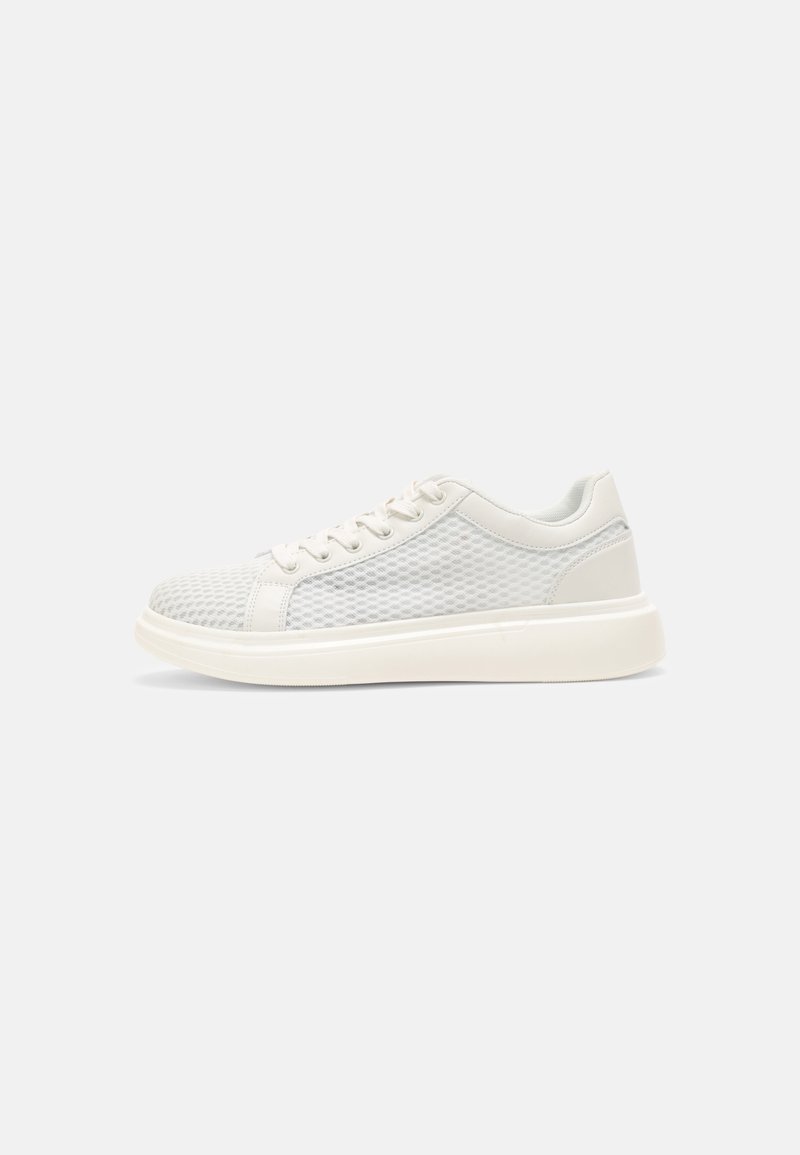 Sneakers basses blanches avec côtés en maille, lacets blancs et semelle blanche épaisse, affichées de profil sur un fond uni.