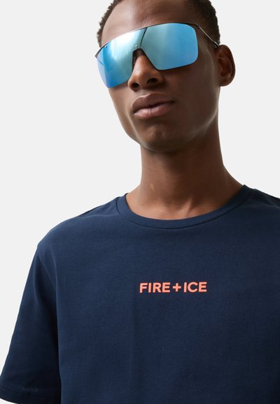 Námorně modré bavlněné tričko s kulatým výstřihem, na přední straně s výrazným oranžovým textem "FIRE+ICE". Model nosí reflexní modré sluneční brýle.