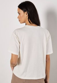 Camiseta de manga corta color crema con escote redondo y corte relajado, con una textura suave y un diseño sencillo.