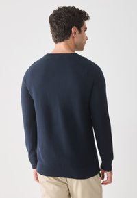 Marine brei trui met een geribde zoom en boorden, voorzien van een ronde hals en textielstof, getoond vanaf de achterkant op een neutrale achtergrond.