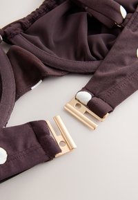 Gros plan d'une sangle en tissu marron foncé avec des pois blancs et une boucle en métal doré partiellement attachée sur une surface claire.