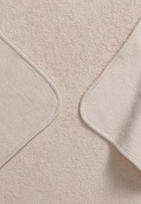 Beige texturerad matta med mjukt, plyschigt yta; rundade hörn har en kontrasterande, slät kant som framhäver dess design och materialkontrast.
