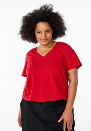 Rode V-hals T-shirt met korte mouwen, gemaakt van zachte stof. Het shirt heeft een ontspannen pasvorm en is gecombineerd met zwarte broek.
