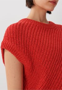 Czerwony sweter z dzianiny, z szerokim dekoltem, krótkimi rękawami i teksturowanym wzorem. Materiał wydaje się miękki, przewiewny i casualowy w stylu.