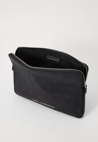 Black zippered pouch made of textured material featuring embossed logos. Interior is lined with fabric, includes a label with brand name.