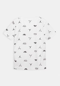 Vit bomullströja med ett heltäckande svart tryck av Jumpman-loggor och text i olika riktningar. Kort ärm och rundad halsringning.