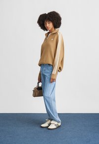 Rjav rebrast pulover z belimi črtami, svetlo modri prugasti kavbojki in bele čevlje. Obleko dopolnjuje majhna rjava torbica.