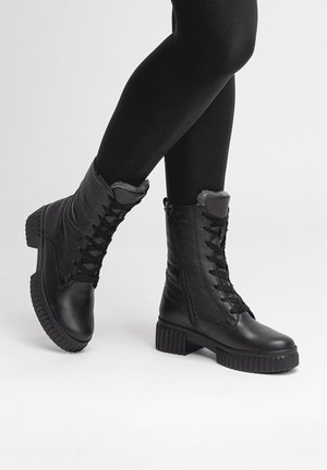 Black lace-up boots with a leather exterior, gray faux fur lining, and chunky rubber soles. Side zipper adds functional detail.